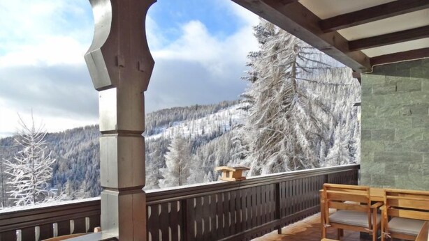 Ein Holzbalkon mit Blick auf schneebedeckte Bäume und ein Berg.