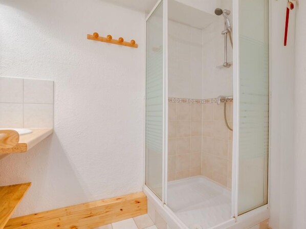 Un baño con ducha, repisa de madera y suelo de baldosas.