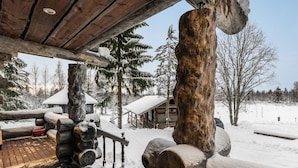 Eine Holzterrasse mit schneebedeckten Baumstämmen und einem rustikalen Haus im Hintergrund.