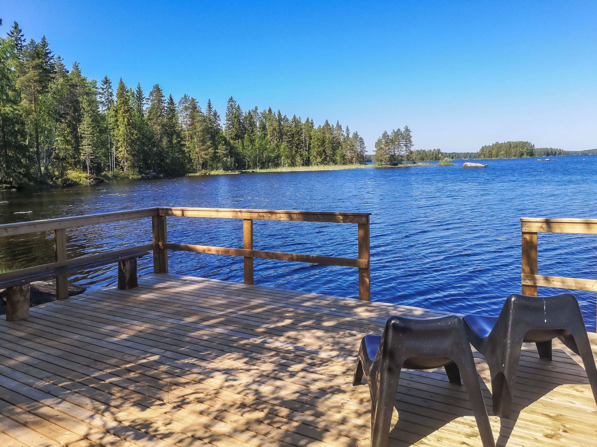 Une terrasse en bois, dotée d’une balustrade, qui offre une vue sur un lac et est entourée d’arbres.
