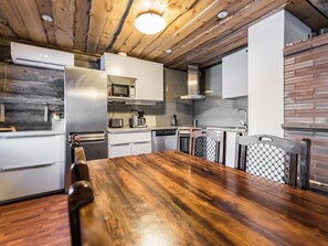 A modern kitchen with a wooden ceiling, stainless steel appliances, and a dining area with a wooden table and chairs.