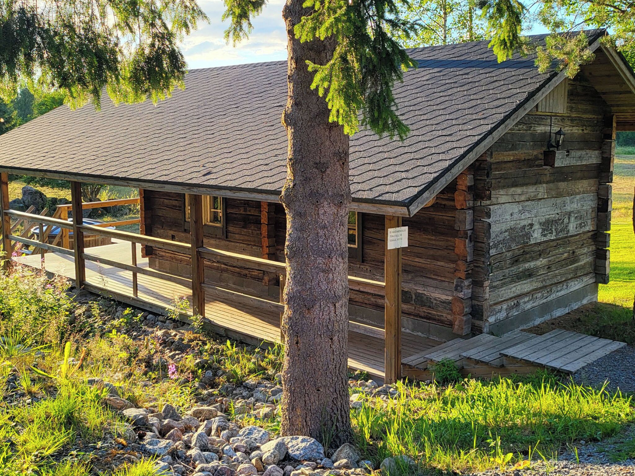 Une cabane rustique en rondins de bois, dotée d’une terrasse en bois et d’un chemin de pierre menant à l’entrée.
