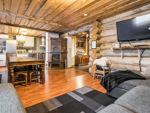 Ein gemütliches Blockhaus-Interieur mit einem Holztisch, Stühlen, einem Kamin, einem an einer Baumstammwand montierten Fernseher und einer Couch.