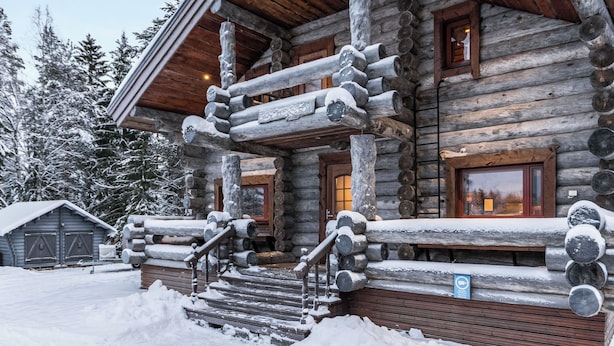 Eine Blockhütte mit einer Holzterrasse, einer Treppe und einer verschneiten Landschaft.
