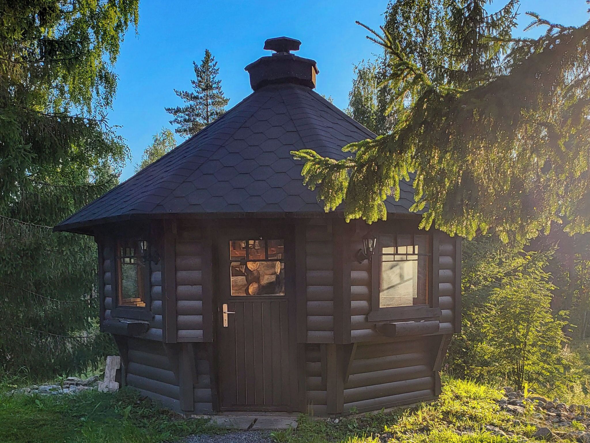 Hirsimökki, jossa on kuusikulmainen katto, savupiippu ja ikkunallinen ovi.