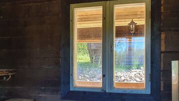 A wooden cabin with a large window, a bench, and a stone wall visible outside.