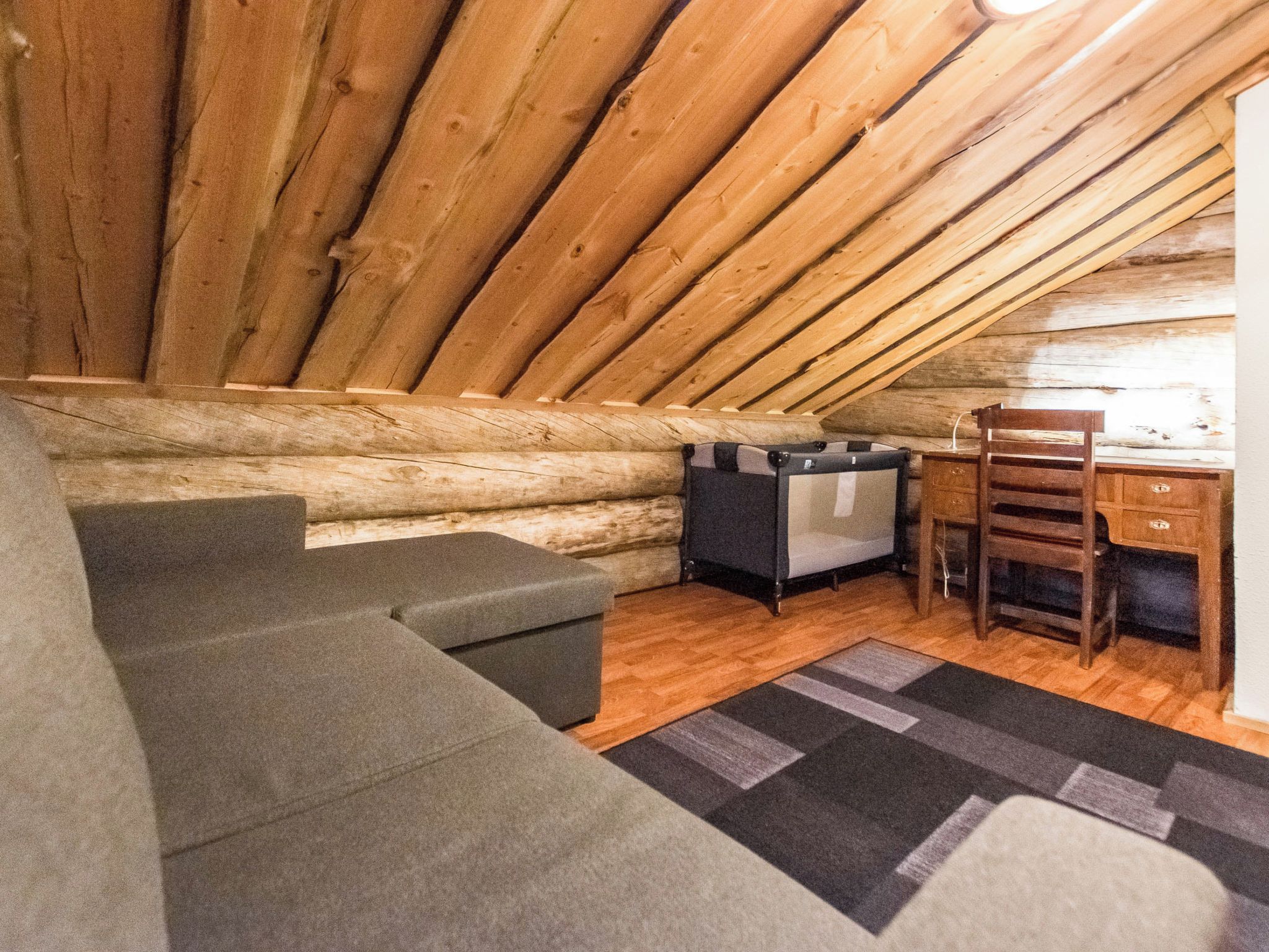 A cozy attic room with a wooden ceiling, a sofa, a chair, and a small desk.