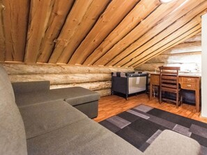 Une pièce mansardée chaleureuse avec un plafond en bois, un canapé, un fauteuil et un petit bureau.