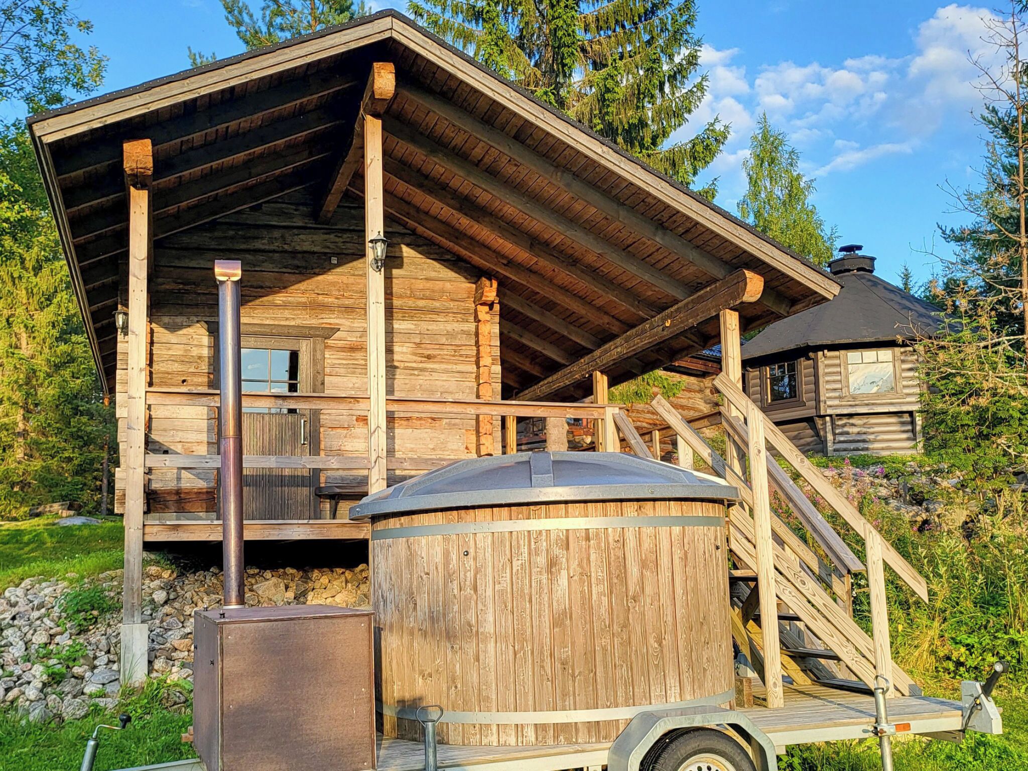 A wooden cabin with a balcony, a chimney, and a metal structure in front.