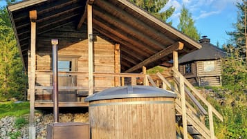 A wooden cabin with a balcony, a chimney, and a metal structure in front.