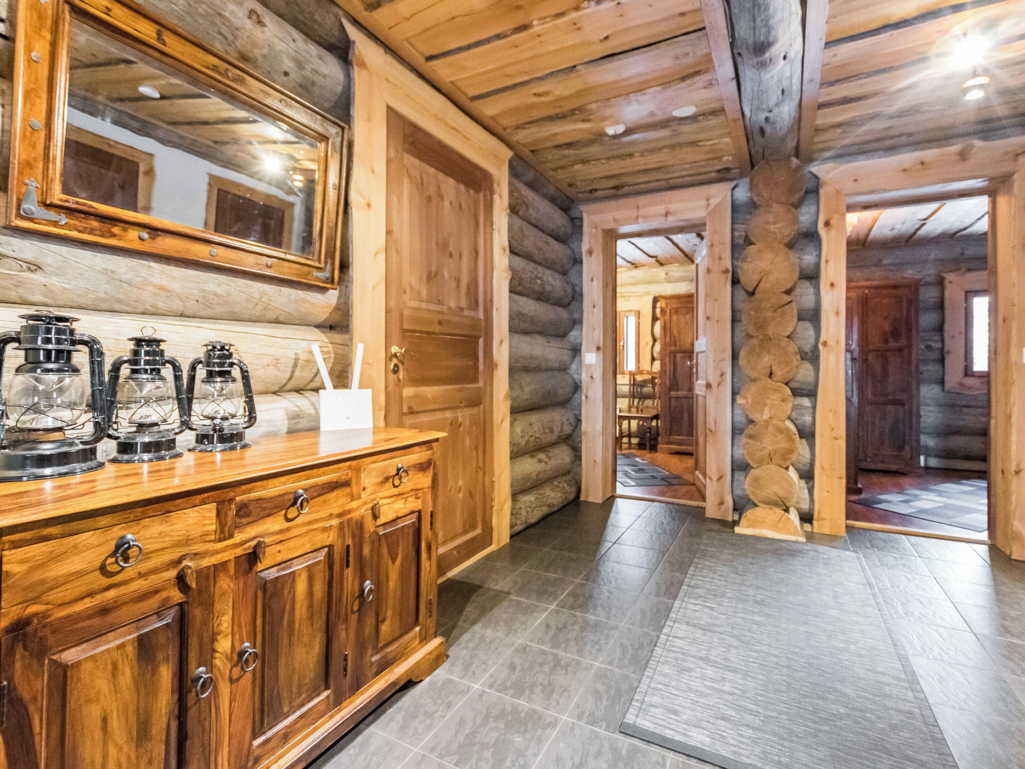 A wooden cabin interior with a large mirror, a wooden cabinet with glass jars, and a log wall.