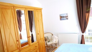 A bedroom with a wooden wardrobe, a chair with a cushion, and a bed with blue bedding.