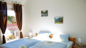 A bedroom with a wooden bed, two nightstands, a window with curtains, and two wall-mounted pictures.