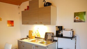 A compact kitchen with a stove, sink, and a toaster on a shelf.