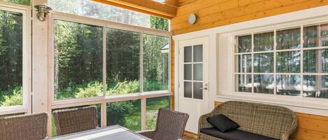 A wooden deck with wicker furniture, large windows, and a view of a forest.