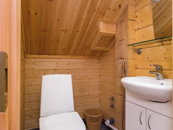 A wooden cabin bathroom with a toilet, sink, and a small trash bin.