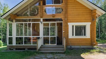 Une cabane en bois à deux étages, dotée d’une véranda, de grandes fenêtres et d’une terrasse bien visible.
