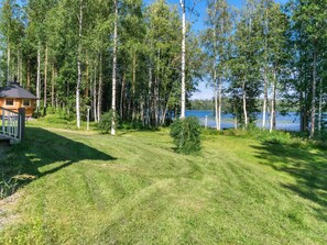 A wooden cabin with a deck, surrounded by a grassy area and tall trees, near a body of water. - Katariina by Interhome (Juva)