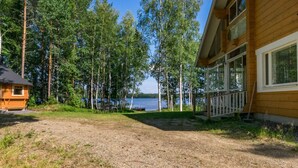 Une cabane avec un chemin de gravier menant à un quai, entourée d’arbres et bordée par un lac.