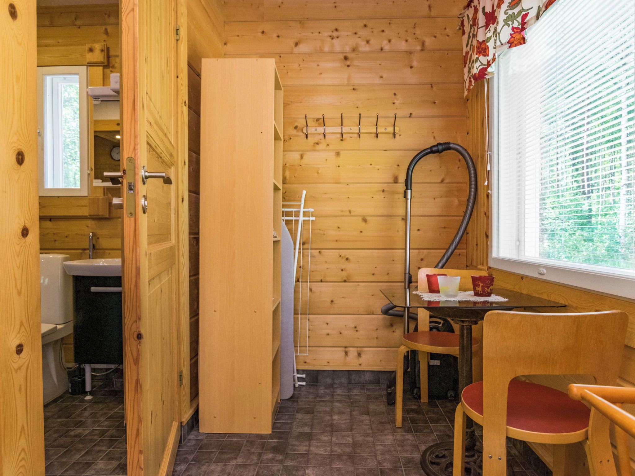 Ein Holzinnenraum mit Bad, Tisch und Stühlen sowie einem Fenster mit Jalousien.