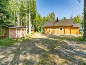 A two-story wooden house with a garage, surrounded by a forested area.