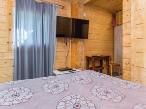 A wooden cabin room with a bed, a television mounted on the wall, and a small table.