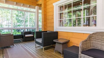 A covered outdoor seating area with wicker furniture and a view of the forest.