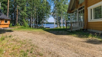 A cabin with a gravel driveway leading to a dock over water, surrounded by trees.