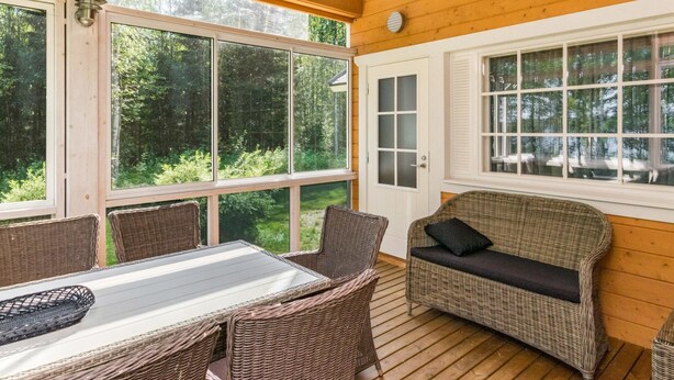 Une terrasse en bois, meublée de meubles en osier, avec de grandes fenêtres et une porte.