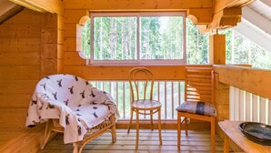 Un chalet en bois accueillant, doté d’une terrasse en bois, d’un espace salon couvert avec une table et d’une grande fenêtre offrant une vue sur la forêt.