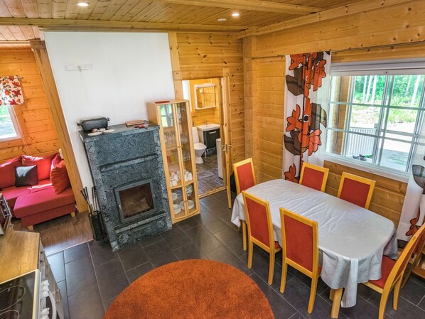 A cozy cabin interior with a fireplace, dining area, and a view of the outdoors. - Katariina by Interhome (Juva)