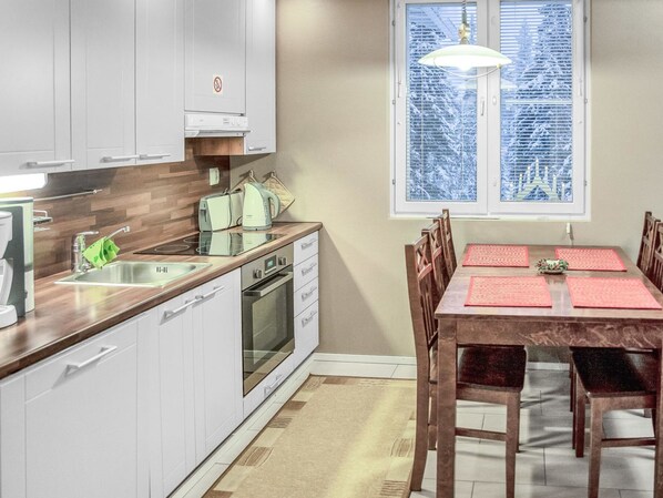 A modern kitchen with white cabinets, a built-in oven, and a dining area with a wooden table and chairs.