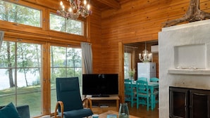 Ein gemütliches Cabin-Interieur mit Fernseher, Holzmöbeln und großen Fenstern mit Blick auf einen See.