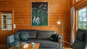 Ein gemütliches Blockhaus-Interieur mit einer Holzwand, einem gerahmten Gemälde, einer Couch, einem Couchtisch und einem Sessel.