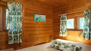 Ein gemütliches Cabin-Zimmer mit Holzwänden, einem Bett mit gesteppter Matratze und Vorhängen mit tropischem Blattmuster.