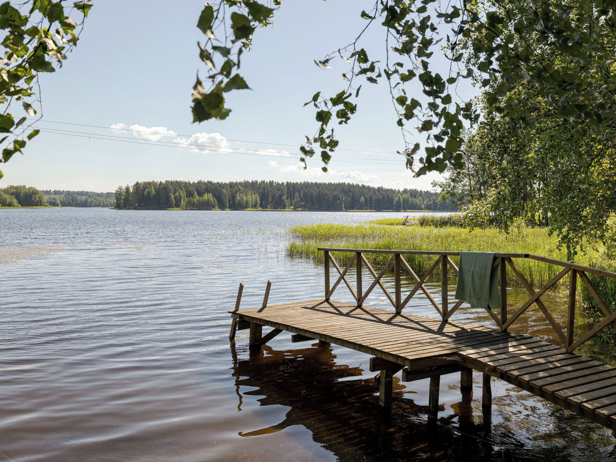 A wooden dock extending into a calm lake with a forested shoreline in the background.