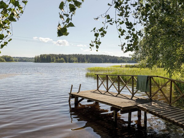 Een houten steiger die uitsteekt in een kalm meer, met een bebost oever in de verte.