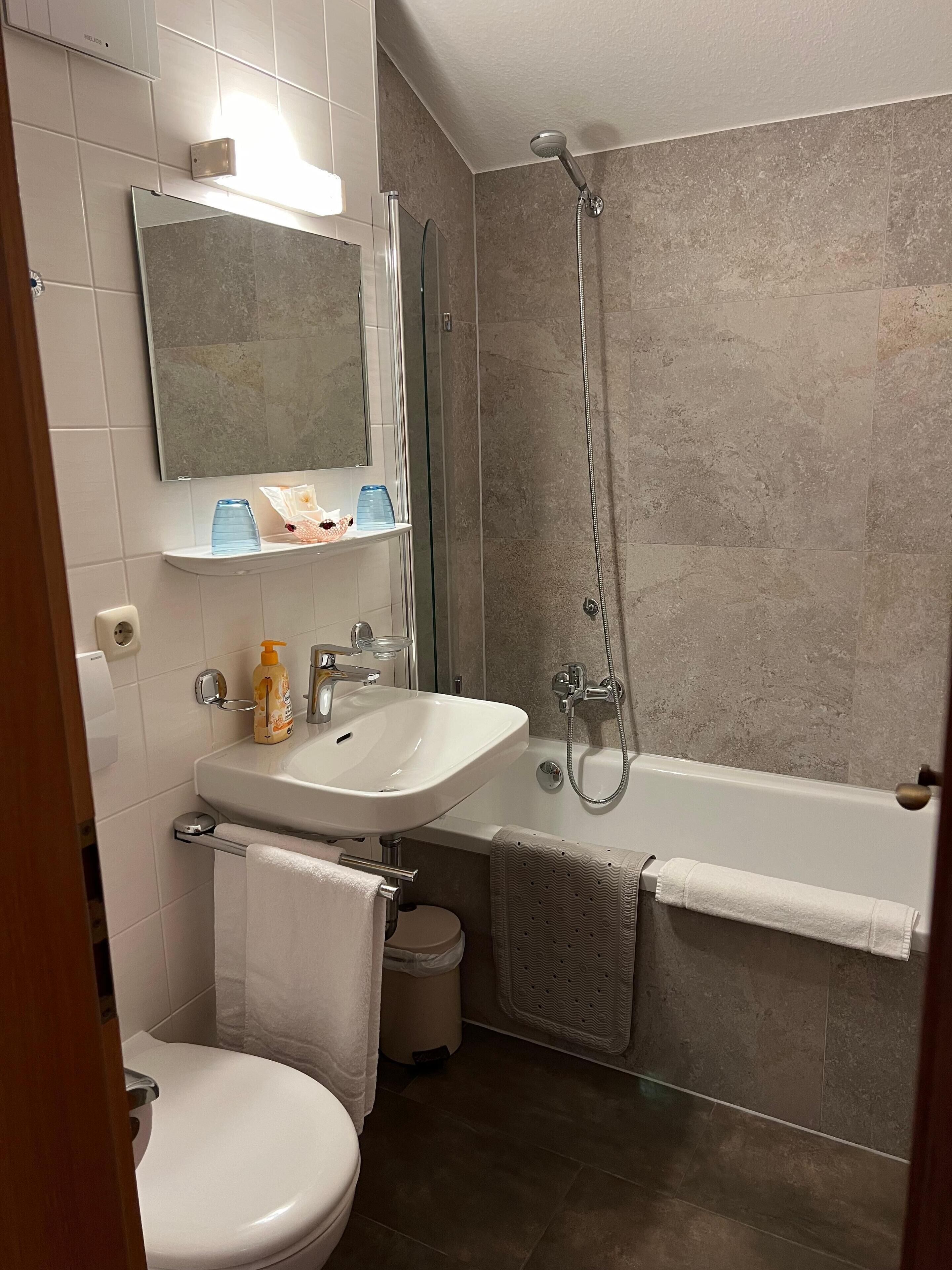 Een badkamer met een wit wastafel, spiegel, toilet en douche.