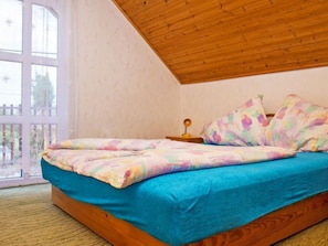 Une chambre avec un plafond en bois, une grande fenêtre offrant une belle vue, un lit avec une literie colorée et une table de chevet avec une lampe.