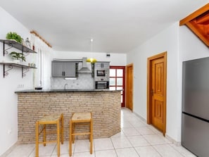 Une cuisine moderne dotée d’un îlot central, de deux tabourets de bar, d’un réfrigérateur et d’une porte en bois.