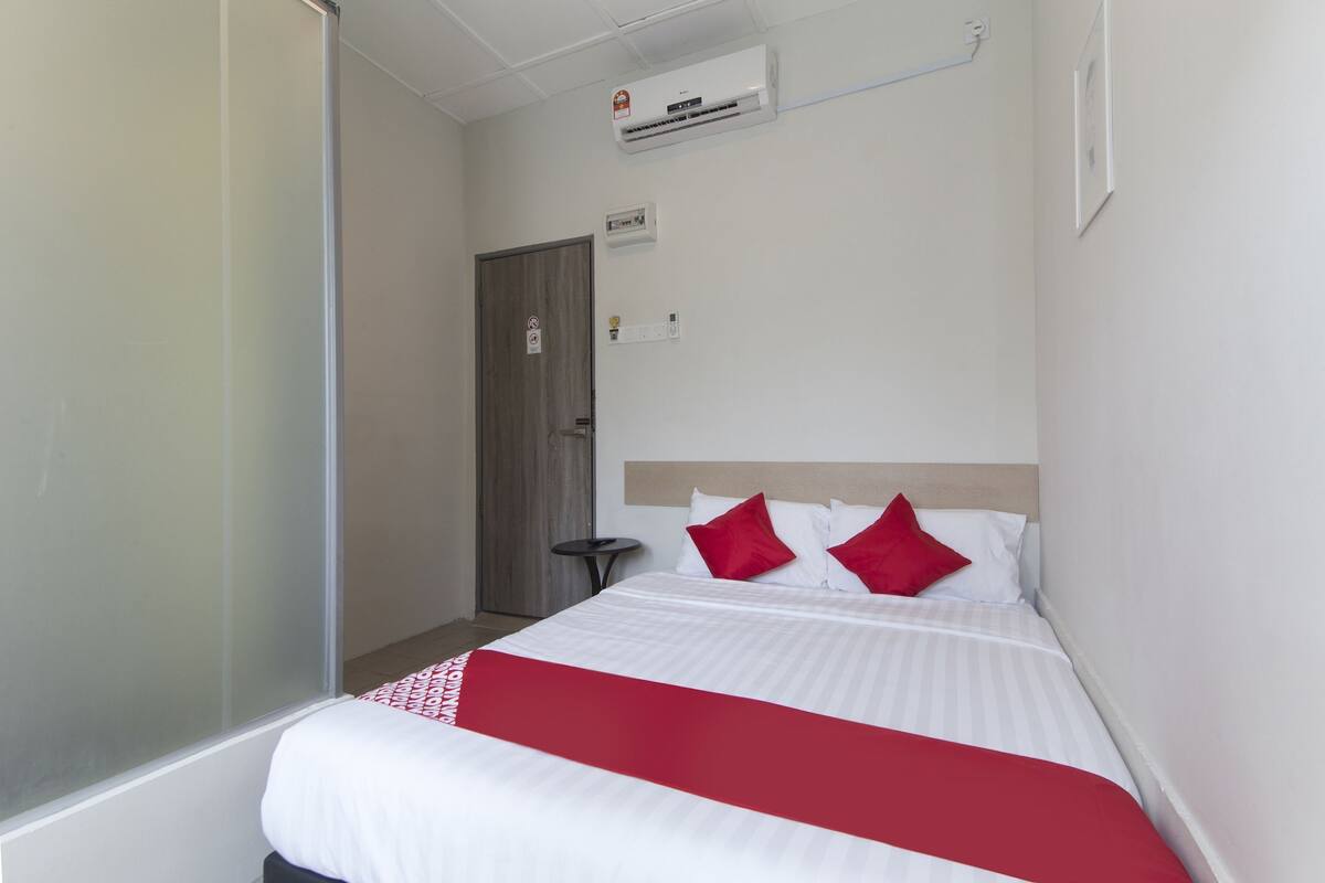 Habitación de hotel con una cama, una mesita, una puerta y un equipo de aire acondicionado en la pared.