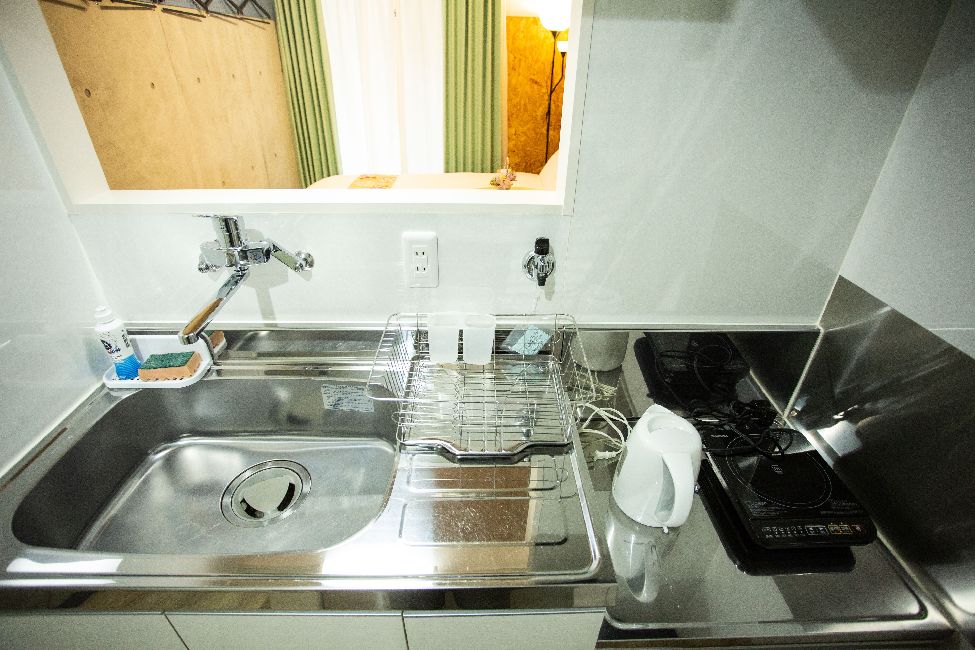 A stainless steel kitchen sink with a dish rack, a white electric kettle, and a black appliance on the counter.