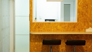 A modern kitchen with a wooden backsplash, a white countertop, and two black bar stools. - Rest inn Kyoto (Kyoto)