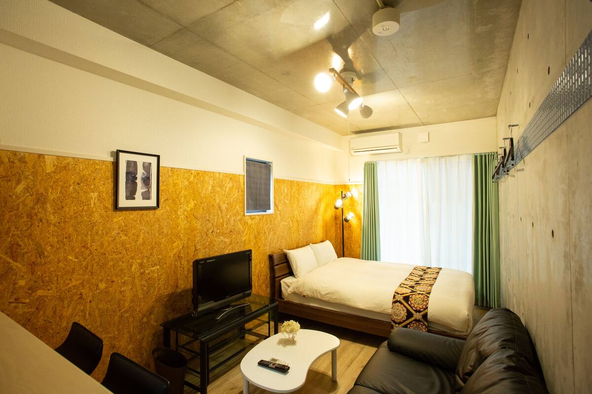 A hotel room with a bed, a TV, a small table, and a sofa.
