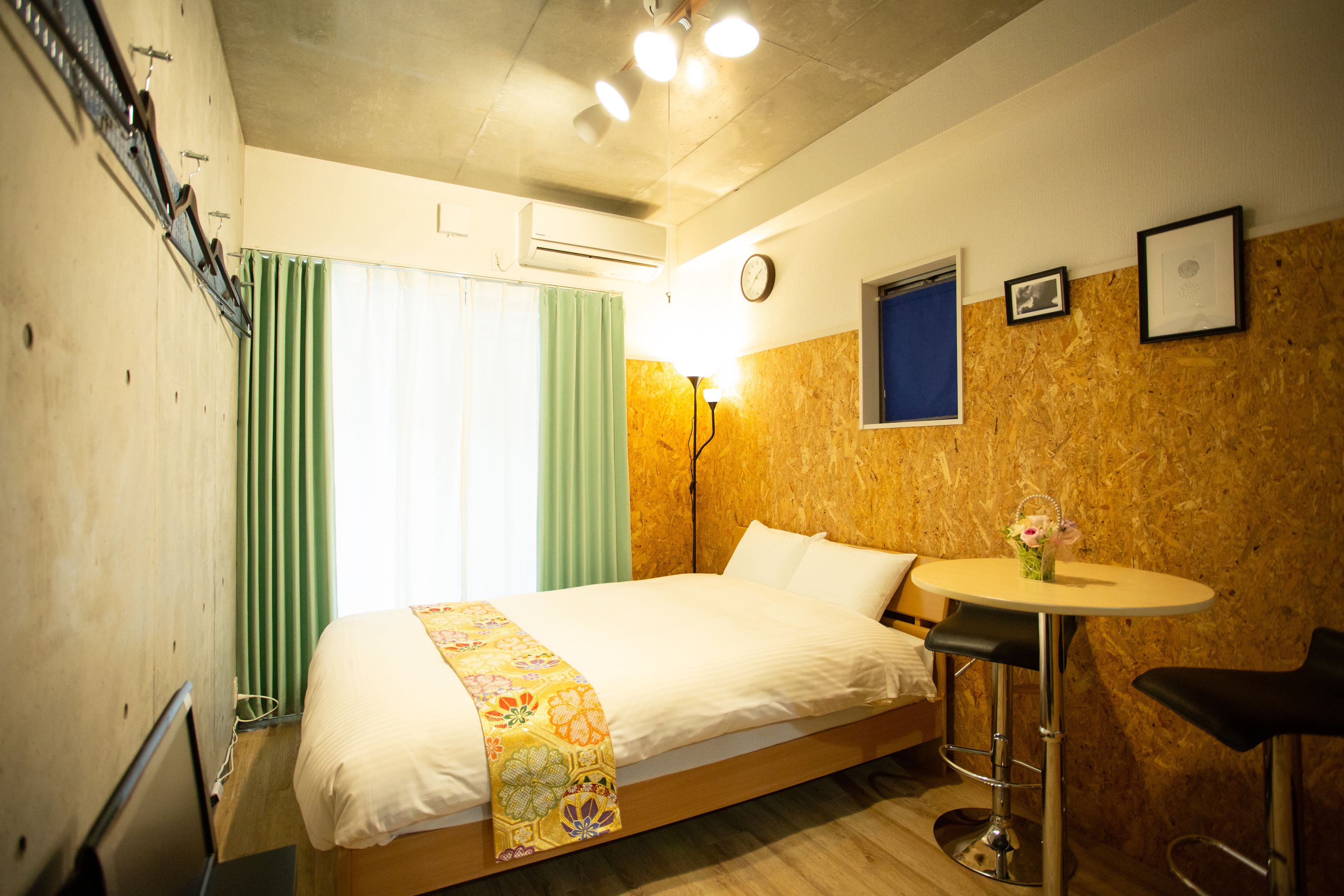 Une chambre d’hôtel avec un lit, une petite table ronde, une chaise, une horloge et une fenêtre avec des rideaux.