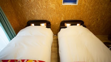 Twee bedden met witte lakens en beddengoed met bloemenprint, een klein raam en een houten wand.