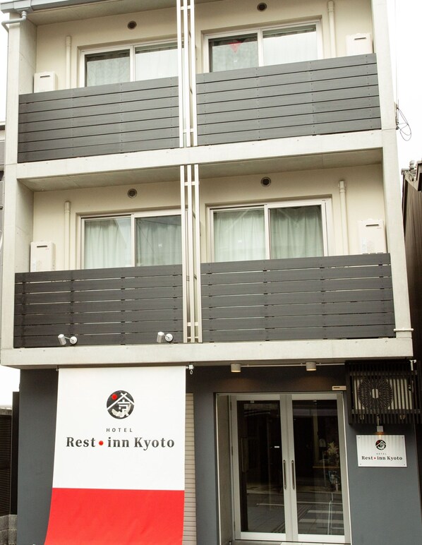 A multi-story hotel with balconies, a signboard for Rest Inn Kyoto, and a glass entrance.