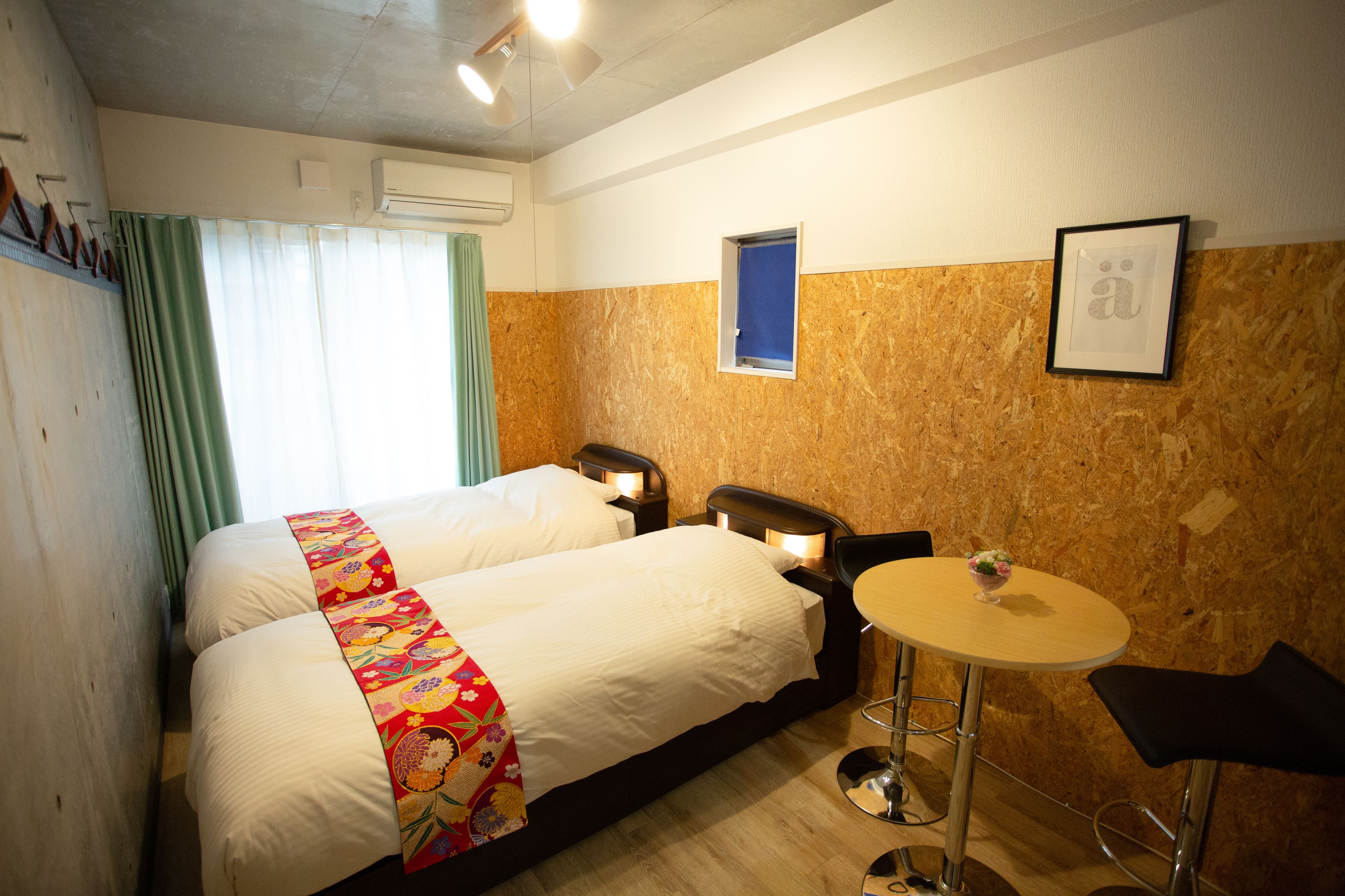 A hotel room with two beds, a small round table, a chair, and a window with curtains.
