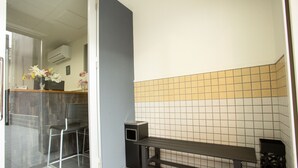 A small, clean room with a bench, a chair, and a small table. There is a tiled wall and a window with a view of the outside. - Rest inn Kyoto (Kyoto)