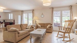 A living room with a sofa, a coffee table, and a rocking chair. There is a kitchen in the background with a refrigerator and a window. - L' amandier by Interhome (Pernes les Fontaines)